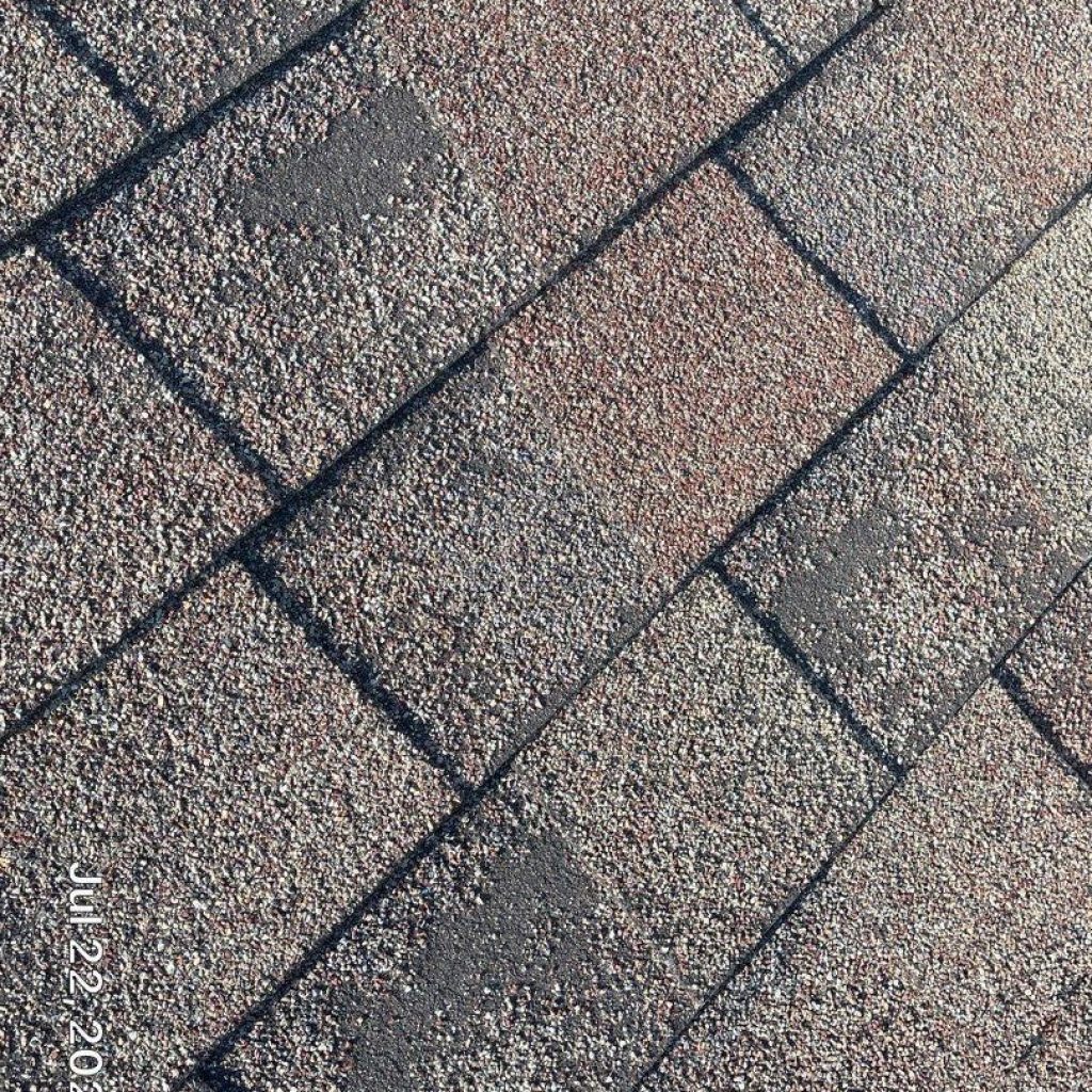 The image displays a close-up view of a textured shingle roof with a pattern of dark and light shades.