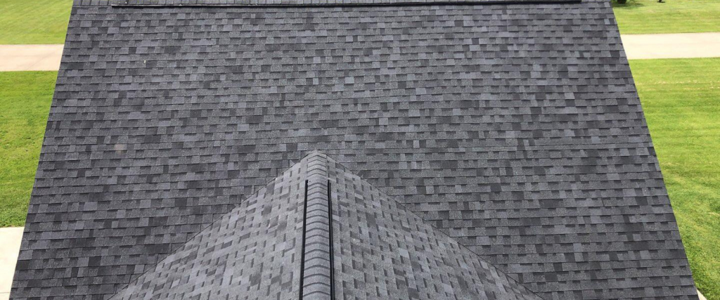 The image shows a symmetrical view down the peak of a house's asphalt shingle roof with a lawn visible in the background.