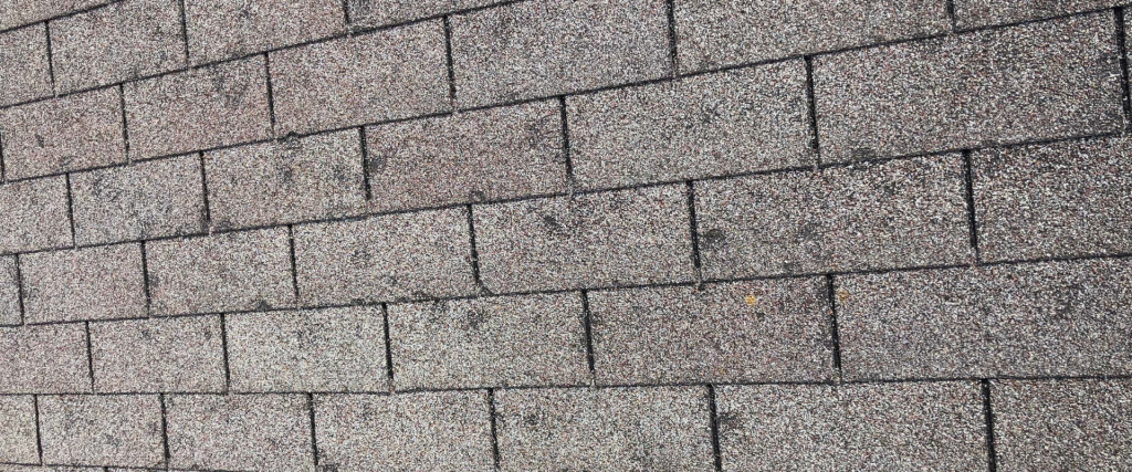 The image shows a close-up view of a textured shingle roof with a pattern of overlapping rectangular tiles.